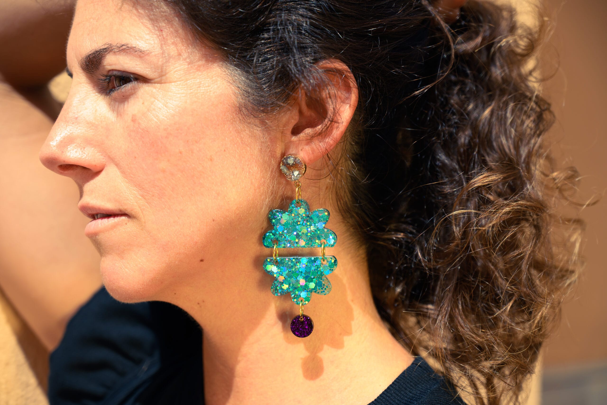 Modelo con pendientes de resina Flor de Caleta: flor turquesa con glitter holográfico y gota morada, hechos a mano en Xàbia