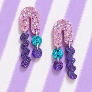 Pendientes asimétricos Tardeo Glitter de resina con arco rosa, onda morada y círculos turquesa sobre fondo de rayas lilas