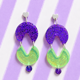 Pendientes neón Comecocos de resina con corazón plateado, pieza morada con glitter y comecocos verde fluorescente sobre fondo de rayas lilas