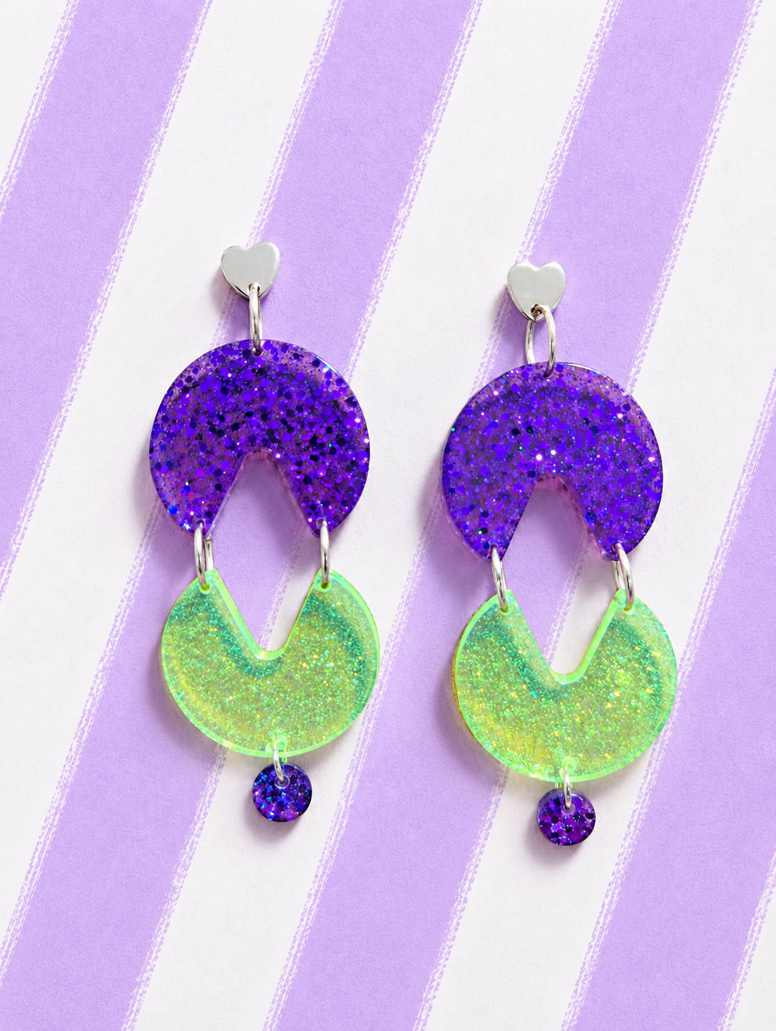 Pendientes neón Comecocos de resina con corazón plateado, pieza morada con glitter y comecocos verde fluorescente sobre fondo de rayas lilas